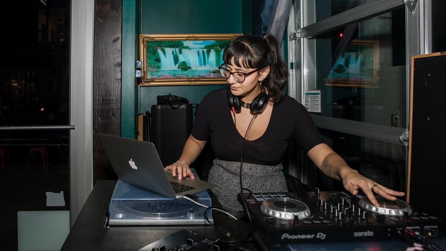 DJ Mami Miami, a Latina DJ, performing with one hand on the controller and one hand on her laptop