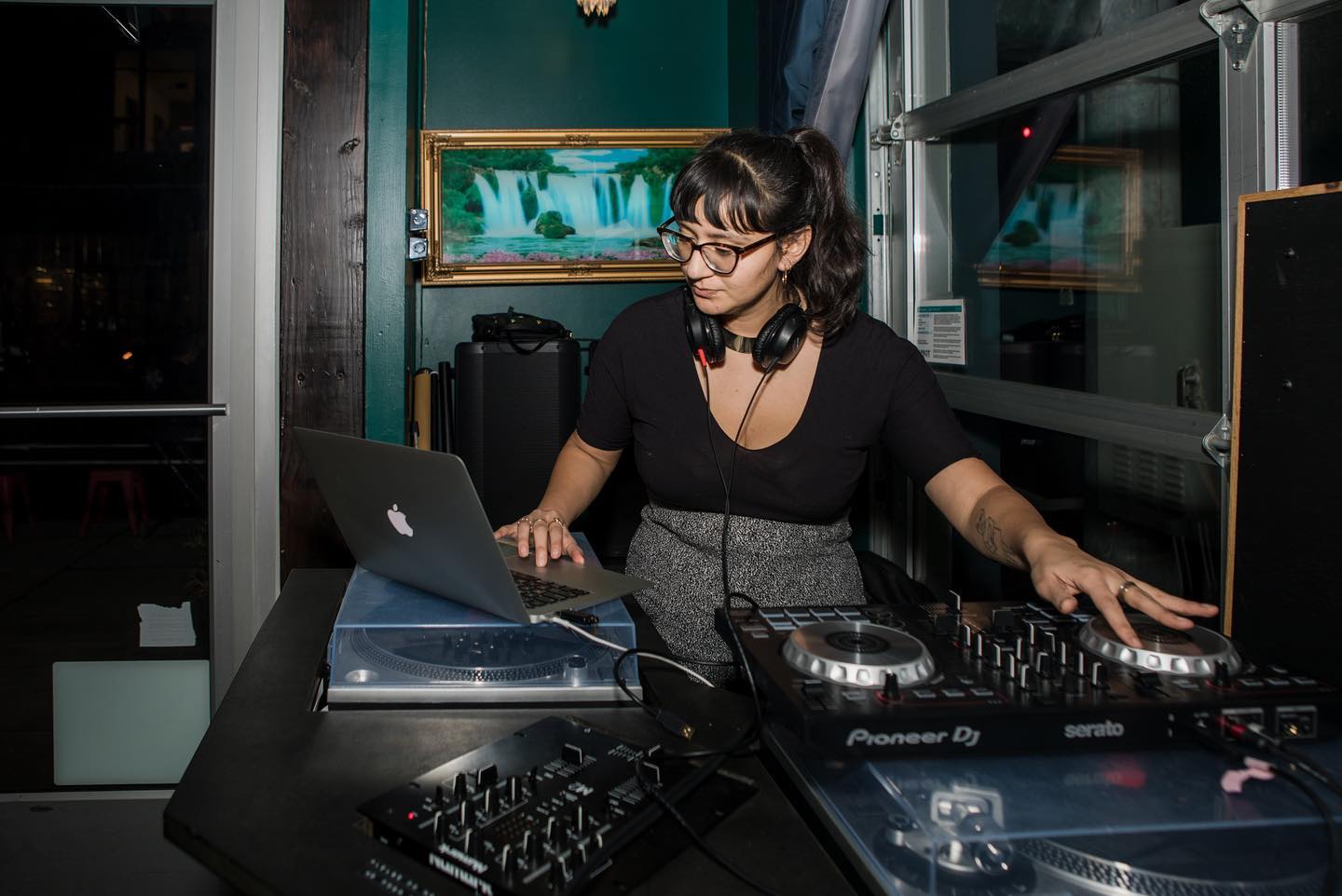 DJ Mami Miami, a Latina DJ, performing with one hand on the controller and one hand on her laptop