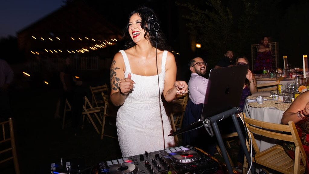 DJ Mami Miami, a Latina DJ, in Bridal Gown with big smile and behind DJ controller decks