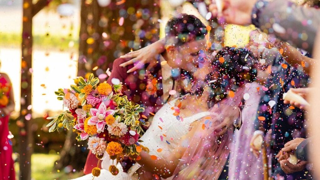 Colorful confetti thrown during wedding kiss down aisle mid-ceremony.