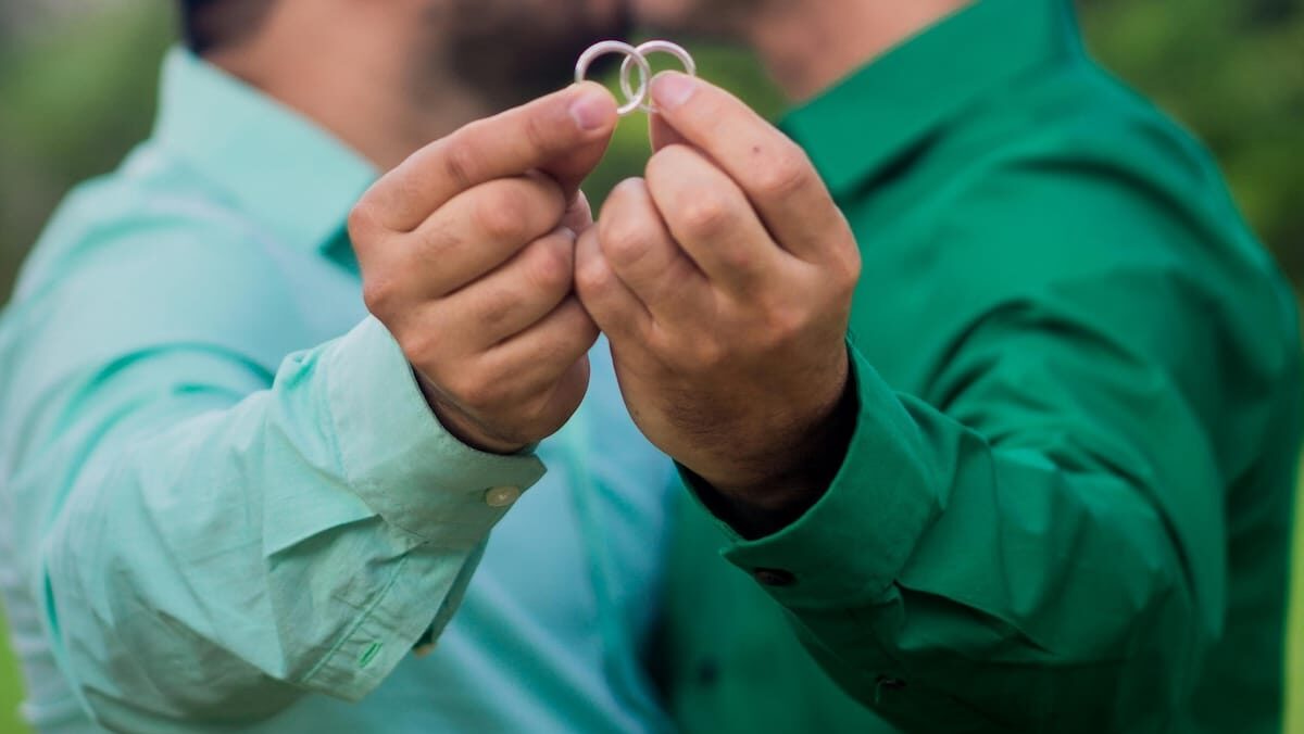 Two grooms hold up their rings to the camera