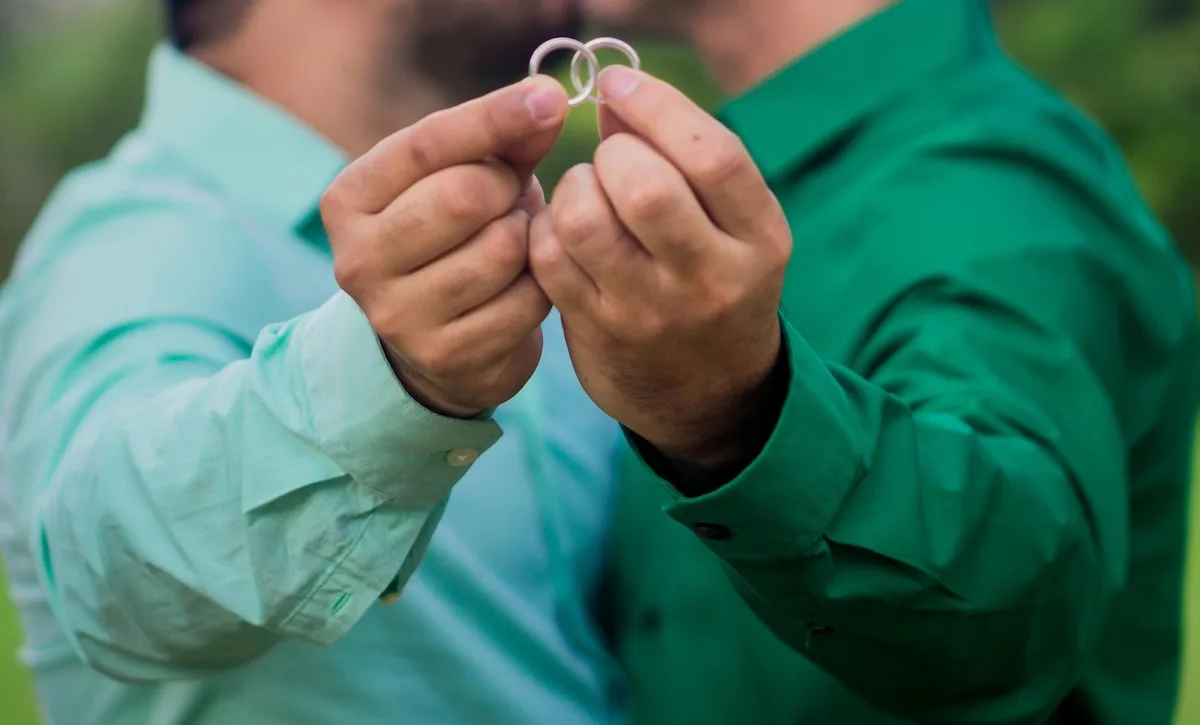 Two grooms hold up their rings to the camera