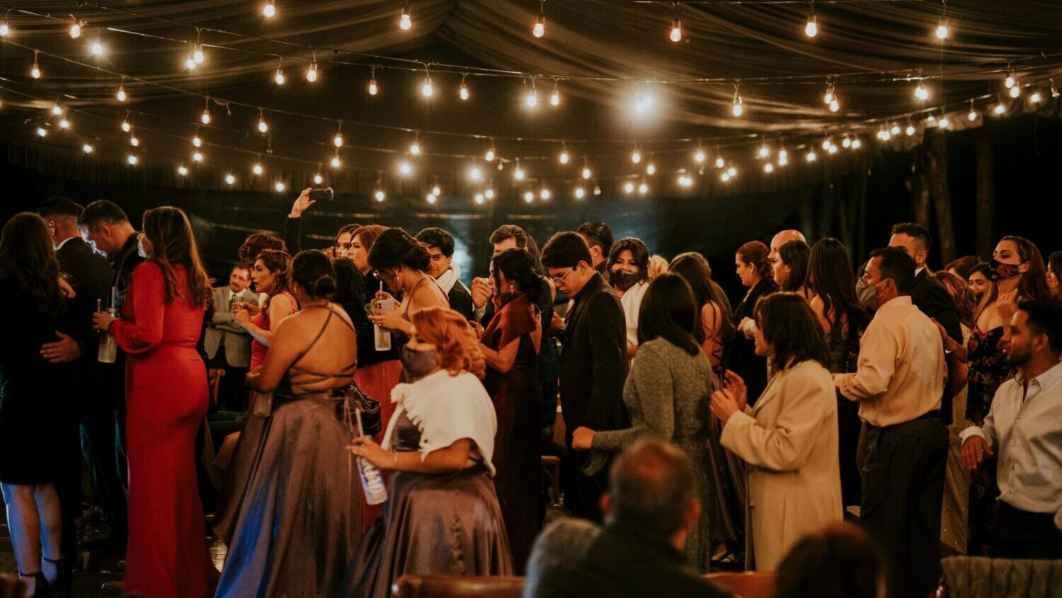 A large crowd of dancers at a wedding reception at night under string lights