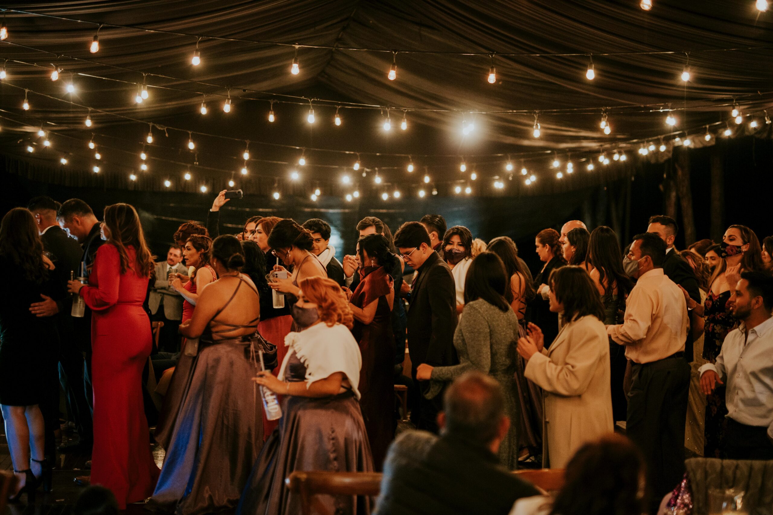 A large crowd of dancers at a wedding reception at night under string lights