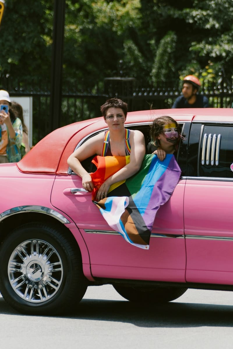 jan-budomo-nwXQ966Z6l4-unsplash Two young teens hold a gay pride flag outside a pink limo, looking off into the distance